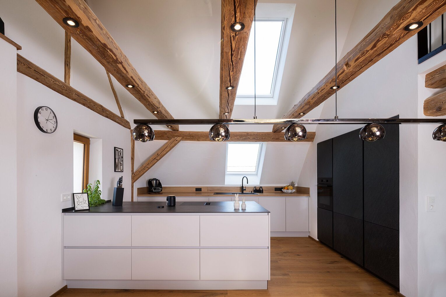 Offene Küche mit Dachschräge von Lorinser Moderne Küche unter Dachschräge mit offenen Balken und großzügiger Arbeitsfläche, umgesetzt vom Küchenstudio Lorinser